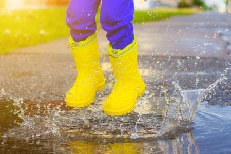 My rubber-booted feet are Bouncing in a puddle. Article about rubber boots. Children's summer shoes. Puddles after rain. Bad weather. A child jumps in a puddle. A happy boy in rubber boots jumps in puddles.の写真素材