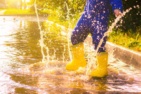 My rubber-booted feet are Bouncing in a puddle. Article about rubber boots. Children's summer shoes. Puddles after rain. Bad weather. A child jumps in a puddle. A happy boy in rubber boots jumps in puddles.の写真素材