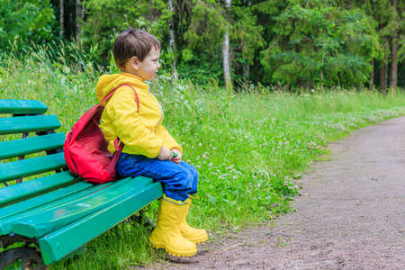 A boy with a backpack is sitting on a bench. School is coming soon. Preparation for school. Studies into the coronavirus. Relax. Copy spaceの写真素材