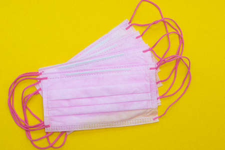 Medical mask isolated on a yellow background. Pink face mask. Article about the second wave of coronavirus. Protection of the respiratory system. Pneumonia and coronavirus. Pandemic.の写真素材