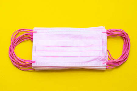 Medical mask isolated on a yellow background. Pink face mask. Article about the second wave of coronavirus. Protection of the respiratory system. Pneumonia and coronavirus. Pandemic. Copy spaceの写真素材
