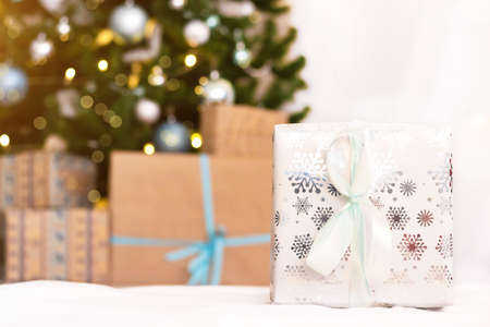Christmas gift on the background of a Christmas tree. New year and Christmas. Copy space. Bokeh from a garland. Festive mood. Choosing a gift for a holiday. Packed gift with a bowの写真素材