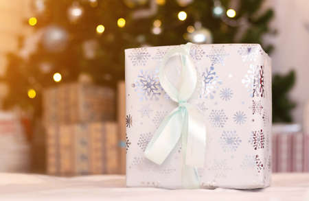 Christmas gift on the background of a Christmas tree. New year and Christmas. Copy space. Bokeh from a garland. Festive mood. Choosing a gift for a holiday. Packed gift with a bowの写真素材