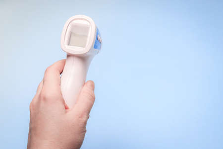 infrared thermometer on a blue background in your hand. the thermometer in his hand. prevention....