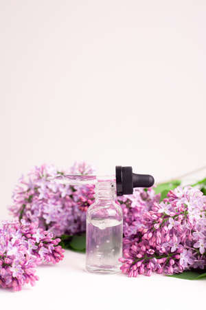 Hyaluronic acid bottle and lilac on a white background. Beauty container. Skin care. Vitamins for the skin. Rejuvenation. Female beauty. An article about the benefits of hyaluronic acid. Article about the choice of hyaluronate. Copy space. A branch of lilac. Flowering. Natureの写真素材