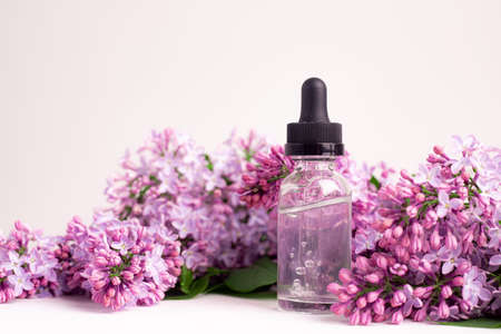 Hyaluronic acid bottle and lilac on a white background. Beauty container. Skin care. Vitamins for the skin. Rejuvenation. Female beauty. An article about the benefits of hyaluronic acid. Article about the choice of hyaluronate. Copy space. A branch of lilac. Flowering. Natureの写真素材