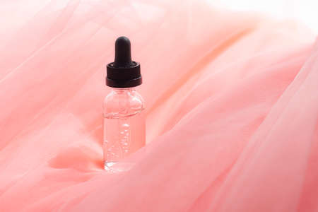 Hyaluronic acid bottle on coral fabric. Beauty container. Skin care. Vitamins for the skin. Rejuvenation. Female beauty. An article about the benefits of hyaluronic acid. Article about the choice of hyaluronate. Copy space.の写真素材