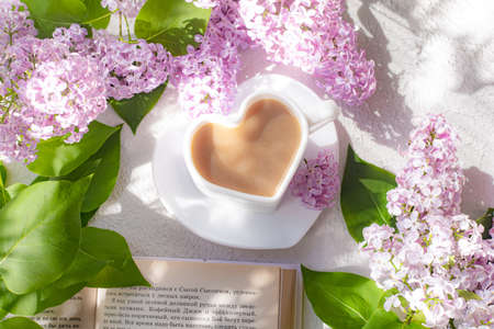 Cappuccino coffee in a cup with a book and a branch of lilac