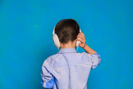 A boy with headphones on a blue background. Children's headphones. Harm of headphones for the child. Useful audiobooks for children. An article about children's leisure. Music. Copy spaceの写真素材