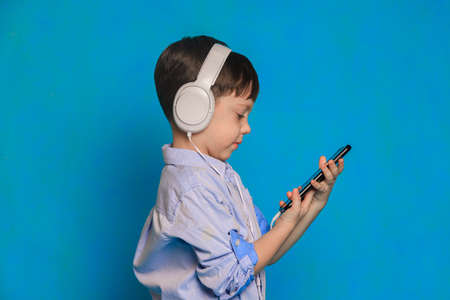 A boy with headphones on a blue background. Children's headphones. Harm of headphones for the child....