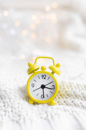 Alarm clock on a plaid with a garland . Yellow alarm clock. Cozy vibes . Home comfort. New Year and Christmas.の写真素材