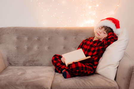 A boy in a Santa hat is reading a book on a lifestyle sofa. Reading books. New Years mood.の写真素材