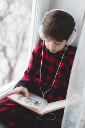 A boy is reading a book on the window. children's books. An article about children's leisure . child developmentの写真素材