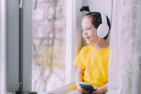A boy with a phone is sitting on a lifestyle window. social media. modern children. An article about developed children. modern technologiesの写真素材