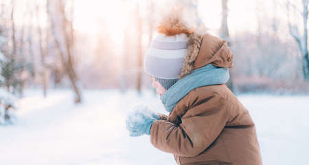 A boy blows snow off his hands winter lifestyle. Winter painting. Snow Park. Cold. Happy childhoodの写真素材