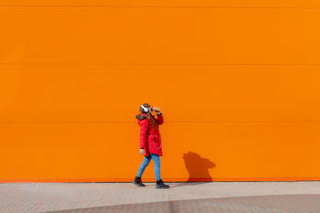 A girl listens to music with headphones on the background of an orange wall. Copy space. Mockup. An article about modern youth. An article about modern music. Article about the choice of headphones. Urban lifestyleの写真素材
