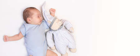 The baby is lying in a crib with a teddy bear . The baby is 0-3 months old. A calm sleeping baby. Healthy baby sleep. An article about toys for kids. A soft toy. Copy space bannerの写真素材