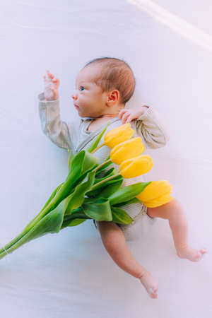 A newborn baby with a bouquet of tulips. A greeting card. March 8th. Baby and flowers. yellow tulipsの写真素材