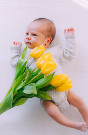 A newborn baby with a bouquet of tulips. A greeting card. March 8th. Baby and flowers. yellow tulipsの写真素材