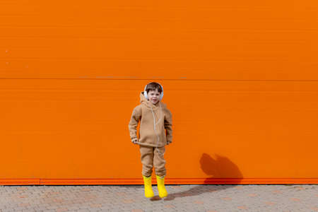 A boy listens to music with headphones on the background of an orange wall . Copy space. Mockup. An article about modern children. An article about modern music. Article about the choice of headphones. Urban lifestyleの写真素材