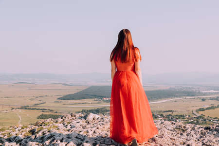 A girl in a red dress on the background of the mountains lifestyle. Illustrating articles about travel. A girl with a beautiful view. Vacation in Crimea. white rock. View of the villages. lifestyle processing. copyspace.の写真素材