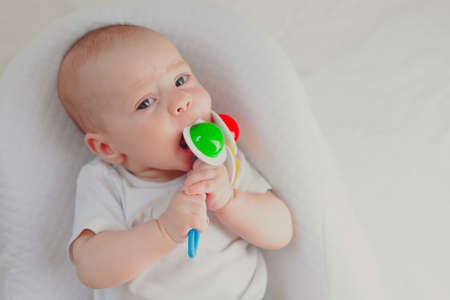 The kid is gnawing on a lifestyle rattle. children's toys. An article about children. An article about children's toys. An article about teething. The rattle is colored. copy spaceの写真素材