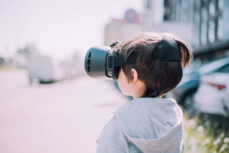 A boy is playing virtual reality glasses on the street. Modern gadgets. children's games. The choice of virtual glasses. An article about virtual glasses. modern children. copy spaceの写真素材