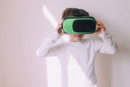 A boy is playing vr glasses on a white copyspace wall . An article about modern gadgets. An article...