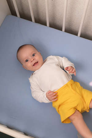 The baby is lying in his crib and looking at the camera. A happy child. children's article. copy spaceの写真素材