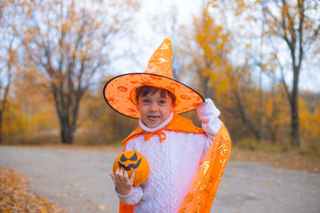 Portrait of a boy in Halloween clothes with a pumpkin on the street . A traditional holiday. October 31.の写真素材