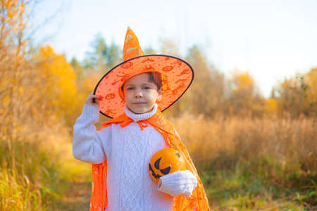 Portrait of a boy in Halloween clothes with a pumpkin on the street . A traditional holiday. October 31.の写真素材