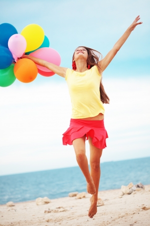 Happy girl holding bunch of colorful air balloons at the beachの写真素材
