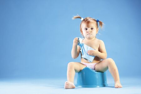 Studio shot of funny toddler sitting on potty chair and playing with toilet paperの写真素材