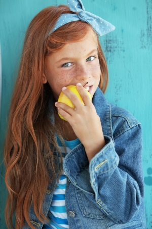 Cute redheaded child eating apple on vintage blue backgroundの写真素材