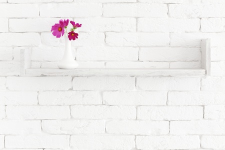 Decorative shelf on white brick wall with flowers in vase on itの写真素材
