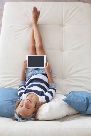 Child playing on tablet pc on the sofa at home, top view pointの写真素材