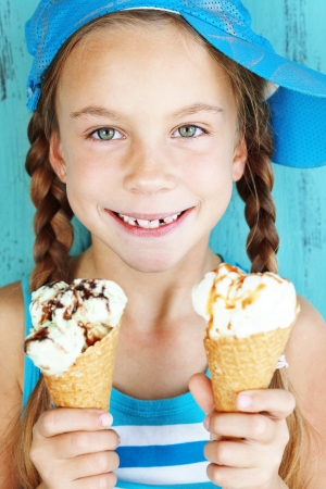 Portrait of 7 years old kid girl eating tasty ice cream over blueの写真素材