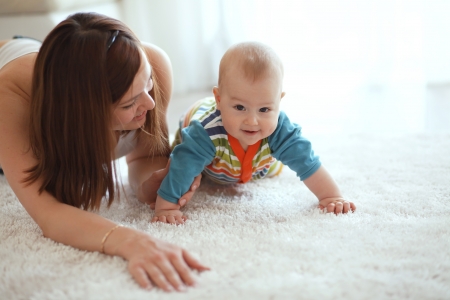 Mother with her baby playing on a carpet at homeの写真素材