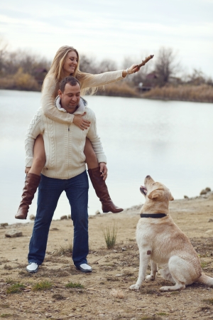 Young happy couple walking with dog near the lake in autumnの写真素材