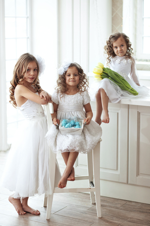 Beautiful little children wearing flower girl dresses posing with the Easter eggs and bouquet of spring tulipsの写真素材