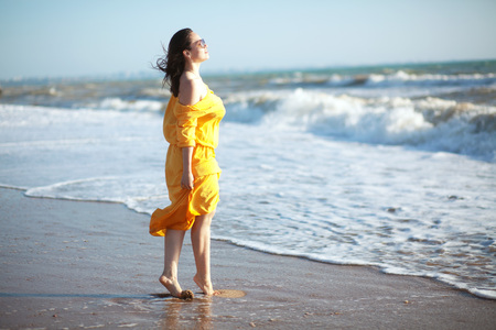Young happy woman wearing yellow dress walking at the coastlineの写真素材
