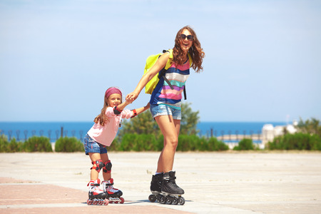 Young mother with her 5 years old daughter rollerskating in parkの写真素材