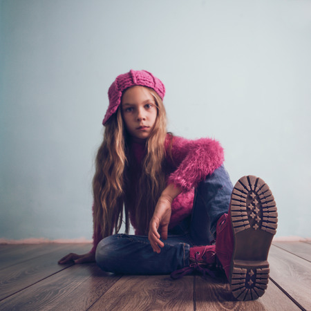 Cute pre-teen girl wearing fashion clothes and shoes sitting on wooden floorの写真素材