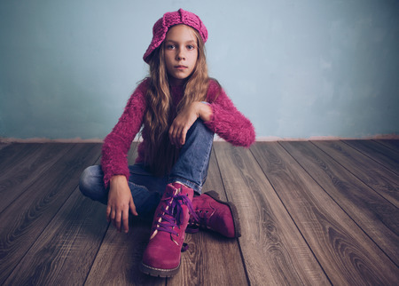 Cute pre-teen girl wearing fashion clothes and shoes sitting on wooden floorの写真素材