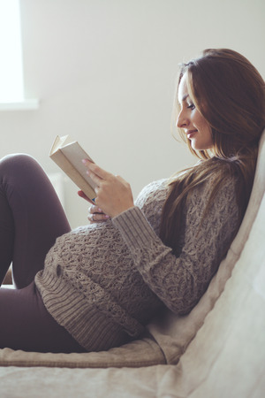 Home cozy portrait of pregnant woman resting at home and reading book on sofaの写真素材