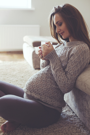 Home cozy portrait of pregnant woman wearing warm cashmere sweater resting at homeの写真素材