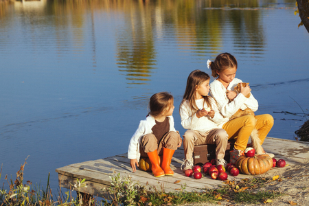 Three cheerful little girls playing on the lake in warm autumn day / Fall lifestyle portrait of children having fun on wooden bearth over the river landscapeの写真素材