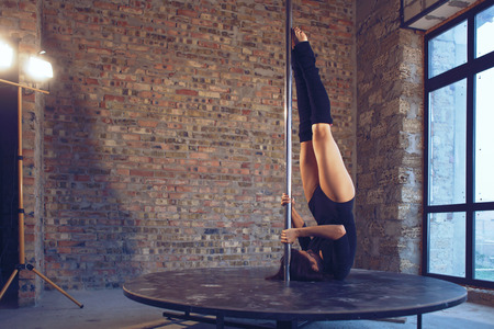 Young pole dancer woman trains on grunge interior with brick wallsの写真素材