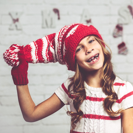 Little fashion girl in fashion Christmas clothes posing over white brick background, full lengthの写真素材