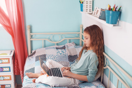 8 years old child having fun using laptop at her bedroomの写真素材